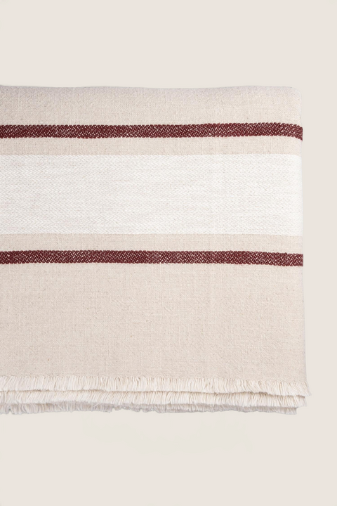 Bolina duk i naturfarget tekstil med hvite felt, røde striper og dekorative frynser langs kanten.