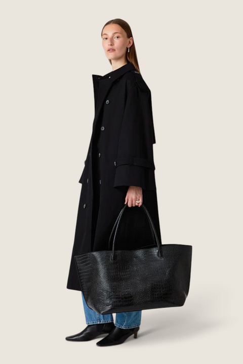 Bolina model carrying a large black leather weekend tote with a croc-embossed finish and long shoulder straps