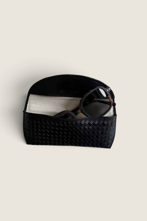 Bolina black woven leather glasses case with a soft interior lining holding a pair of tortoiseshell sunglasses