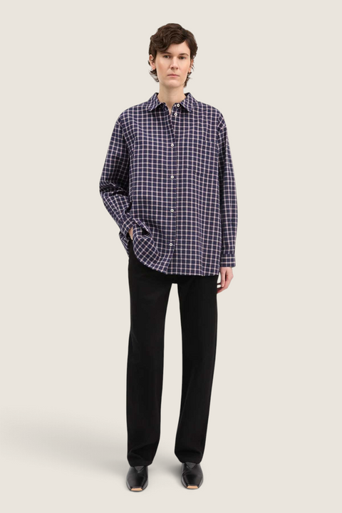 Model wearing a Bolina oversized navy, white, and red check organic cotton poplin shirt with black trousers.