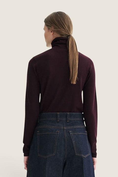 Bolina Korinella merino wool turtleneck sweater in deep burgundy, worn with dark blue jeans, back view.