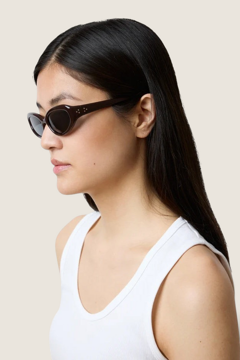 Bolina LIÉ STUDIO Robyn cat-eye sunglasses in dark burgundy worn by a woman in a white tank top, side profile view.