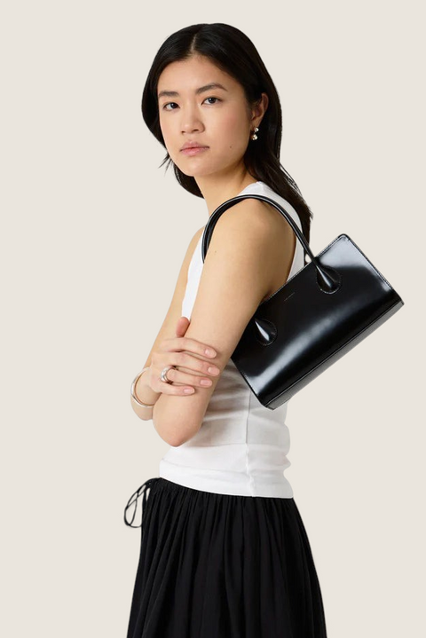 Bolina Lou bag in black patent leather with a slim, elongated shape and glossy finish worn over the shoulder