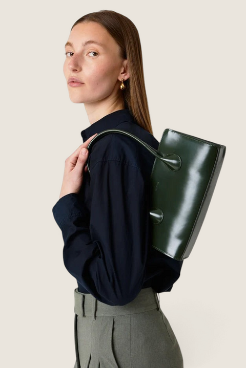 Bolina Lou patent leather shoulder bag in olive green with a sleek, elongated design worn by a model.