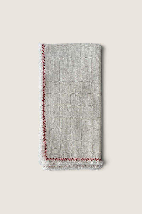 Bolina natural cotton napkin with a textured grid pattern, raw edges, and decorative red stitched border.