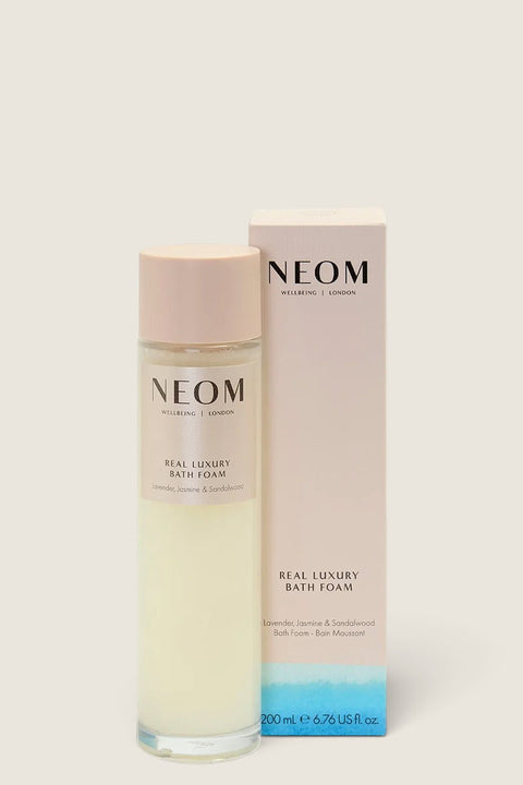 Bolina Neom Real Luxury bath foam in a clear bottle with a pale pink cap next to its matching product box.