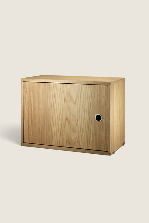 Bolina oak cabinet with a hinged door for String System, featuring a minimalist design and circular handle.