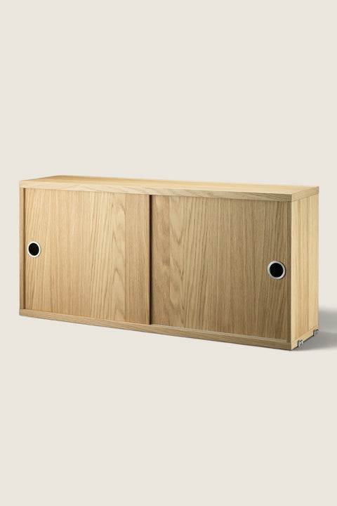 Bolina oak veneer cabinet with sliding doors for String System, featuring a minimalist design and circular handles.