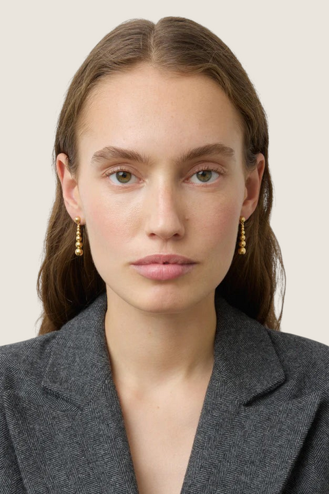Bolina Rebecca gold drop earrings featuring polished spheres of varying sizes worn by a model in a grey blazer.