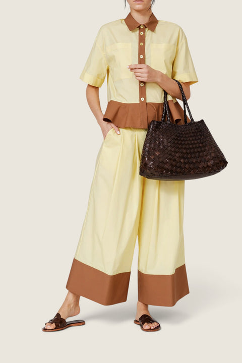 Bolina Santa Croce dark brown woven leather tote bag with an open top design held by a model in a yellow outfit.
