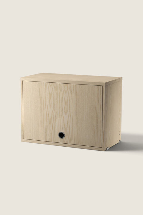 Bolina String System flip door cabinet in ash wood veneer with a minimalist design and circular handle detail.