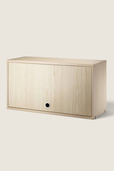 Bolina String System flip door cabinet in light ash wood veneer with a minimalist design and circular handle.