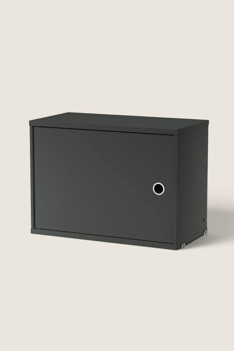 Bolina String System dark grey cabinet with a single hinged door and circular handle for wall-mounted storage.