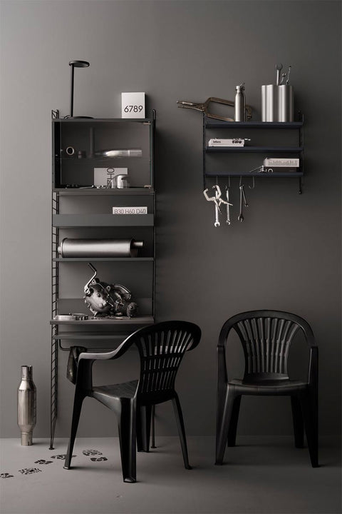 Bolina String System dark grey metal shelving unit with wall-mounted shelves, storage cabinet, and two black chairs.