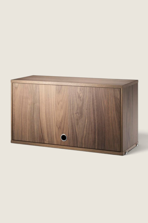 Bolina String System flip door cabinet in walnut veneer with a minimalist design and circular handle detail.
