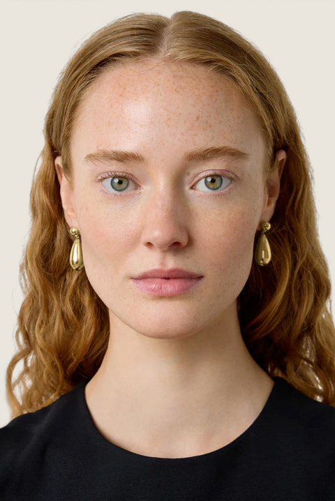 Bolina The Lola gold teardrop earrings worn by a model with long wavy hair, featuring a polished metallic finish.