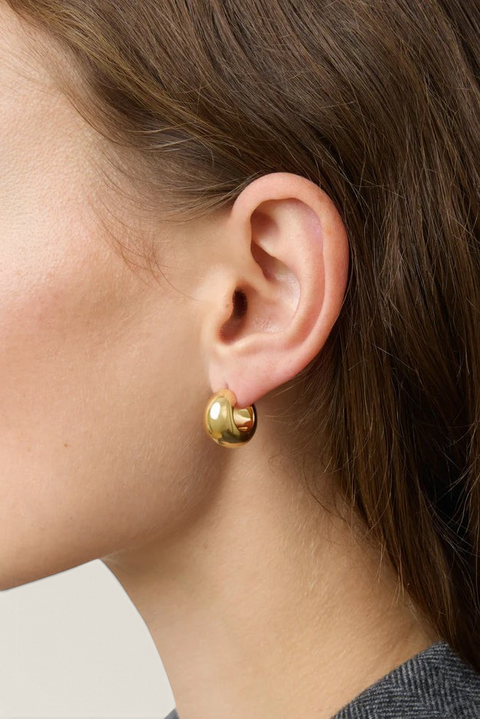 Bolina The Simone gold hoop earrings with a polished, rounded, and chunky design worn on a woman's ear.