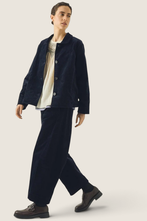 Model wearing Bolina TOAST dark navy corduroy trousers with a barrel-leg fit and twisted seams in a cropped length.