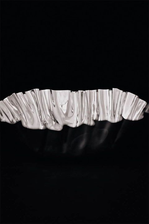Bolina Tydra bowl in mirror polished stainless steel with a wavy, water-like design on a black background.