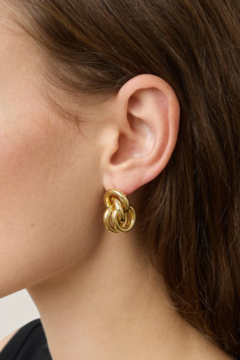 Bolina Vera gold knot-style earrings with a sculptural, rounded design worn on a model's ear.